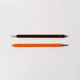 Zwei „Mechanical Pencil – mit der Biene“ von Le Typographe liegen parallel auf einer weißen Fläche. Der obere Bleistift ist dunkelbraun, der untere leuchtend orange. Beide haben glatte silberne Spitzen und kleine Metallkappen, perfekt zum Skizzieren von Grußkarten- oder Grußkarten-Designs.