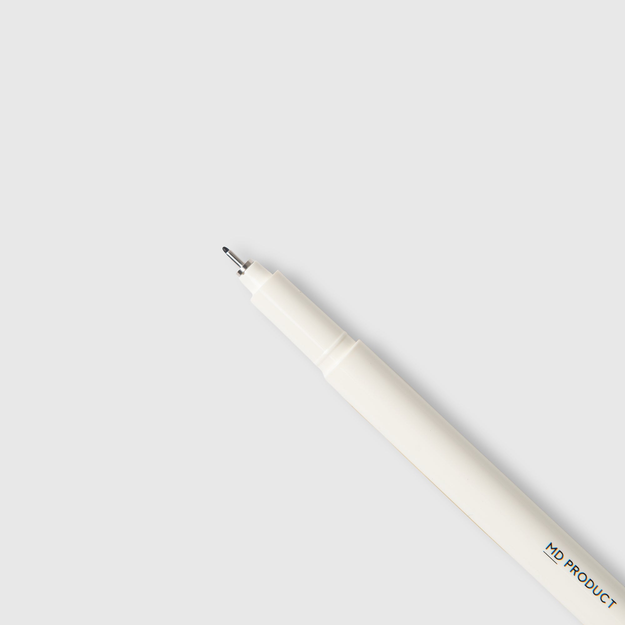 Ein weißer Midori MD Drawing Pen mit feiner Spitze ist diagonal vor einem hellgrauen Hintergrund platziert. Dieser Stift, der die für die Marke Midori typische Qualität aufweist und mit hochwertiger Pigmenttinte auf Wasserbasis gefüllt ist, trägt am hinteren Ende die Aufschrift „MD PRODUCT“.