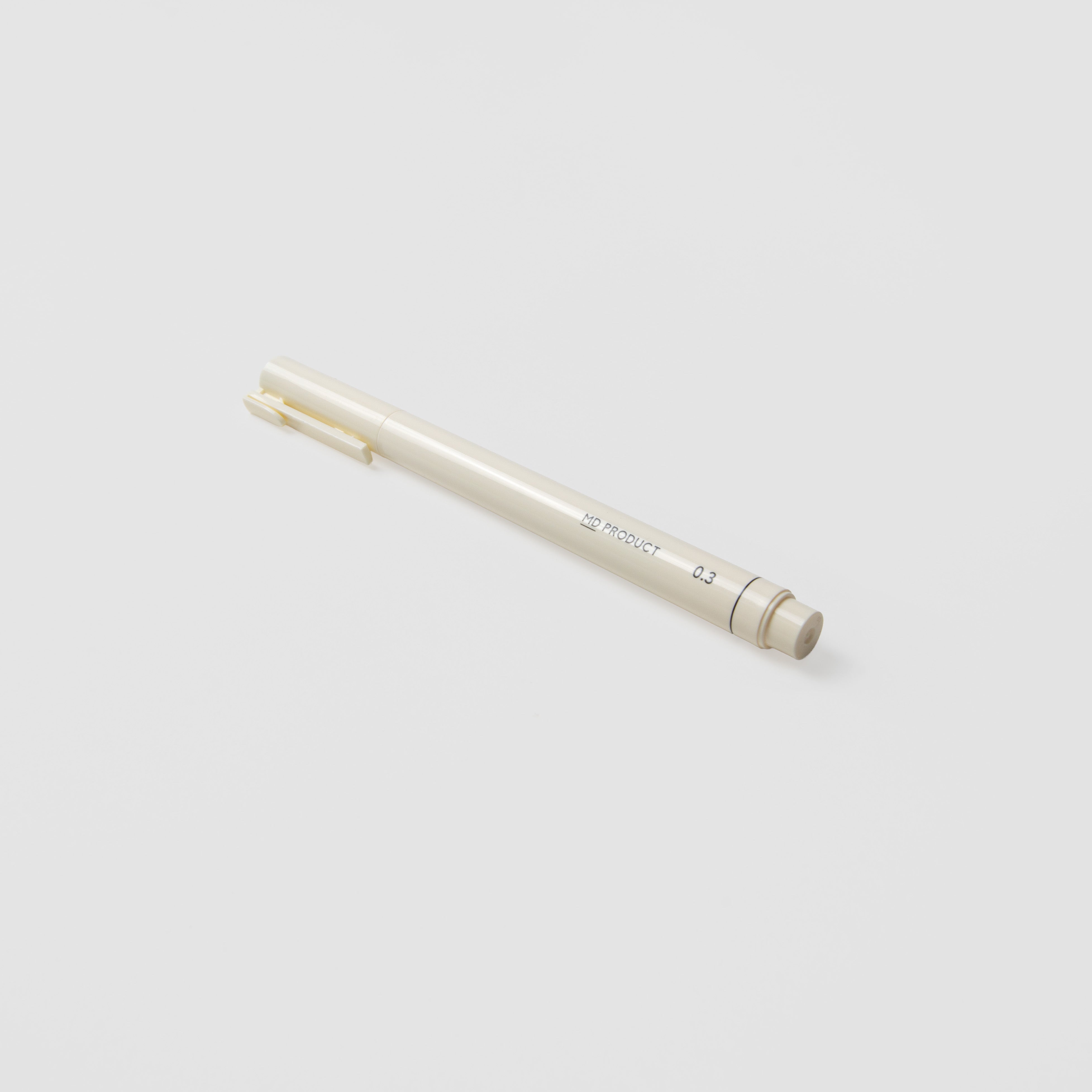 Der beigefarbene Midori MD Drawing Pen 0,3 mm mit Clip ruht diagonal auf einer weißen Oberfläche. Der schlanke Stift mit Kappe ist mit kleinem Text bedruckt und verwendet Pigmenttinte auf Wasserbasis für ein flüssiges Schriftbild.