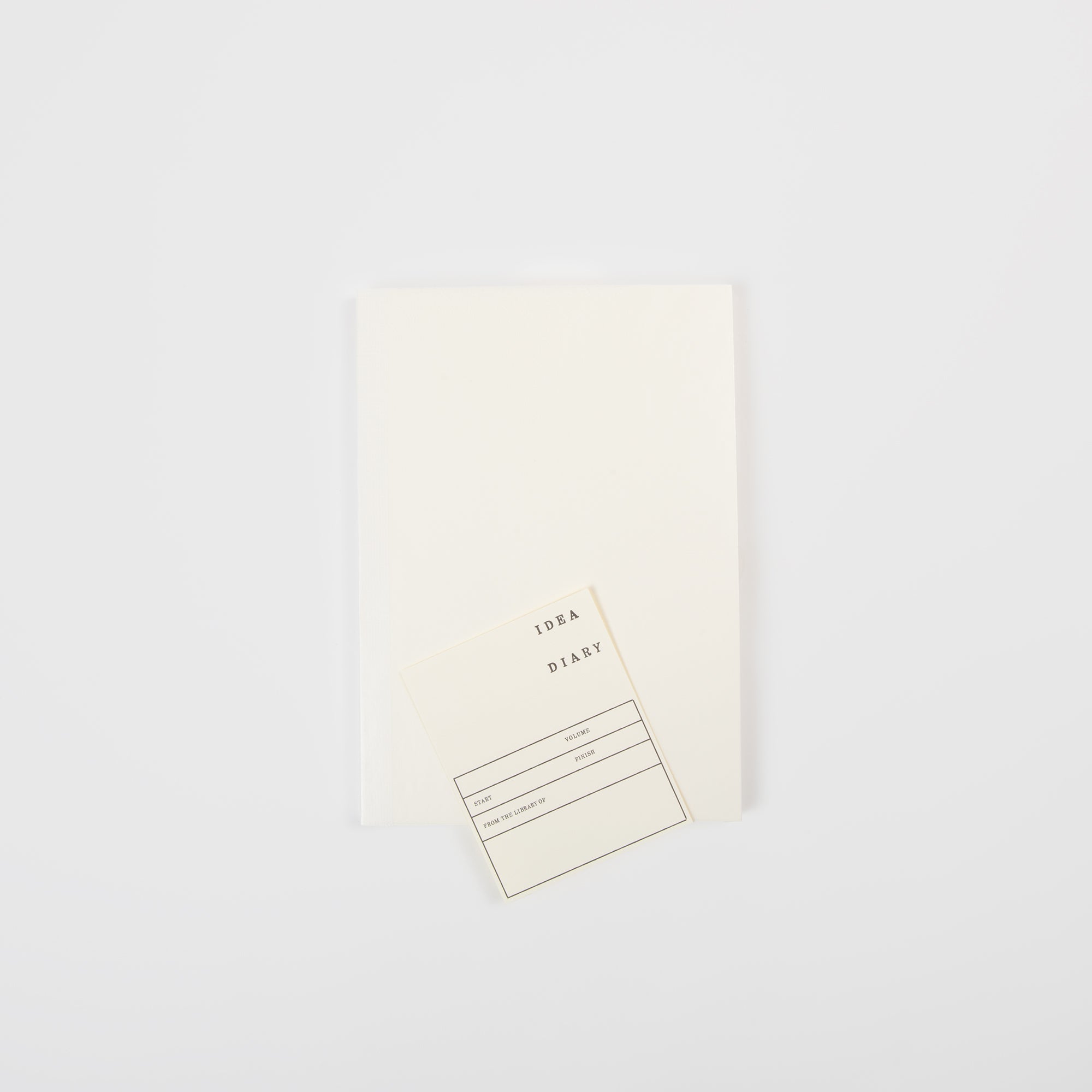 Ein schlichtes, weißes Midori MD Notizbuch A5 mit einer kleinen, cremefarbenen "IDEA DIARY"-Karte auf der Oberseite, die auf weißem Hintergrund steht. Das hochwertige MD-Papier und die klassische Fadenbindung sorgen für ein angenehmes Schreibgefühl.