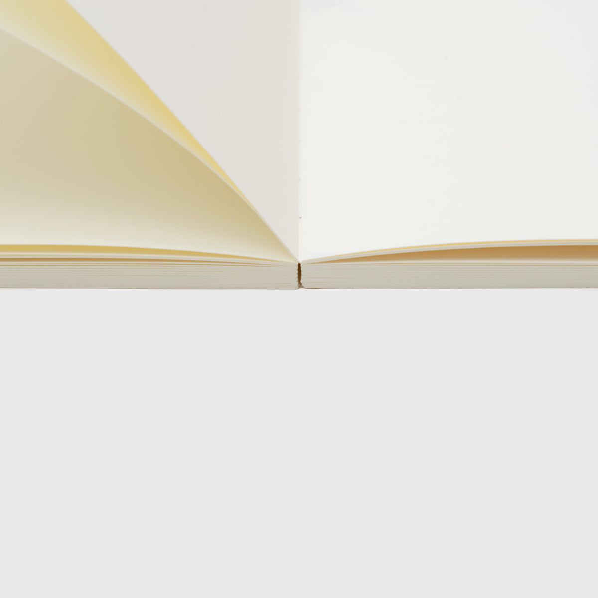 Ein Midori MD Notebook Thick – A5 Square, Blanko liegt von der Seite betrachtet offen und flach da, wobei sich seine cremefarbenen Seiten aus 141 g/m² MD-Papier vor einem weißen Hintergrund fächerförmig ausbreiten – perfekt als Skizzenbuch.