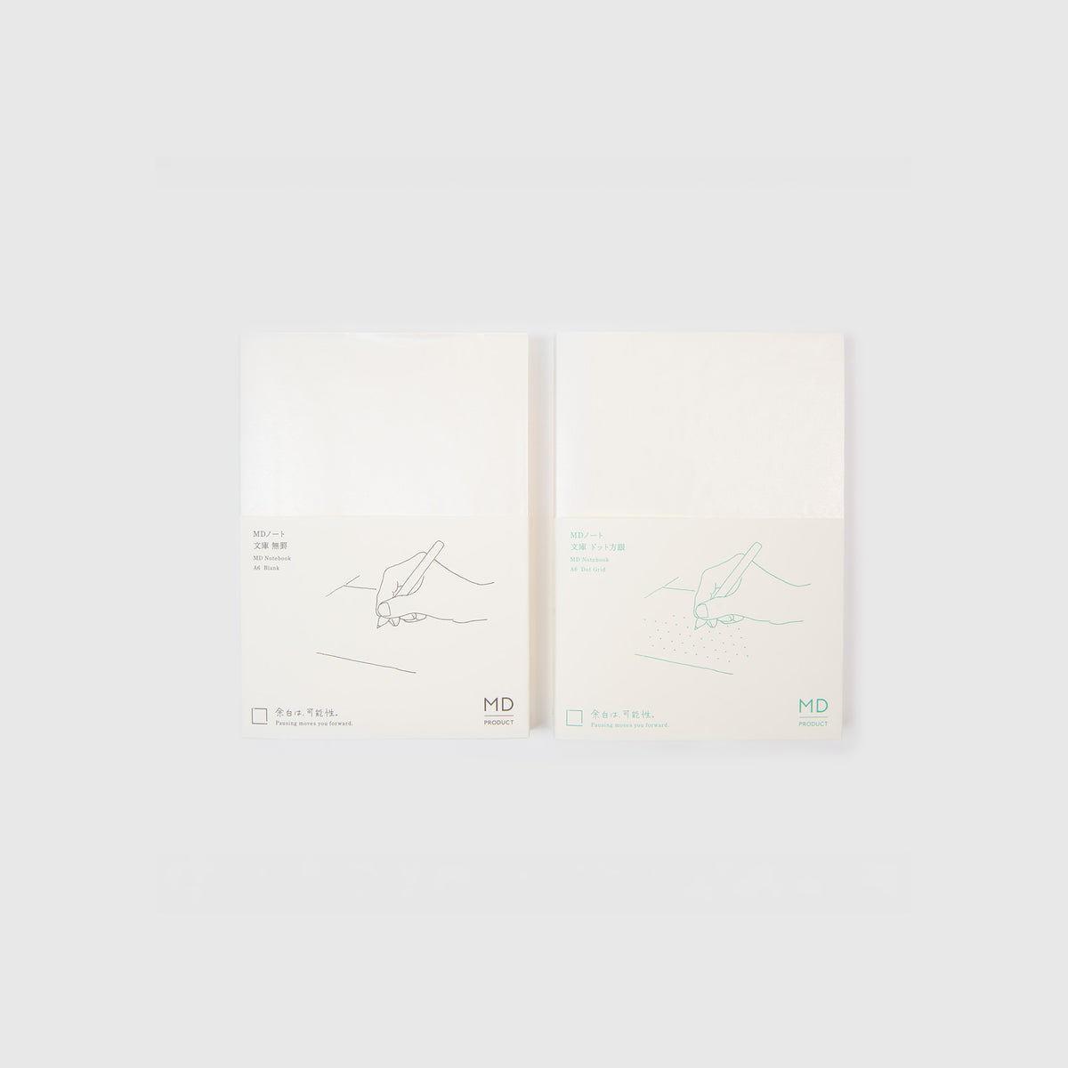 Zwei weiße Midori MD Notebook A6-Notizblöcke in minimalistischer Verpackung, jeweils mit einer schlichten grünen Strichzeichnung einer schreibenden oder zeichnenden Hand. Das Midori MD Paper Notebook-Logo und ein japanischer Text sind am unteren Rand jedes Notizblocks zu sehen und unterstreichen die elegante Fadenheftung, die dem Ganzen einen klassischen Touch verleiht.