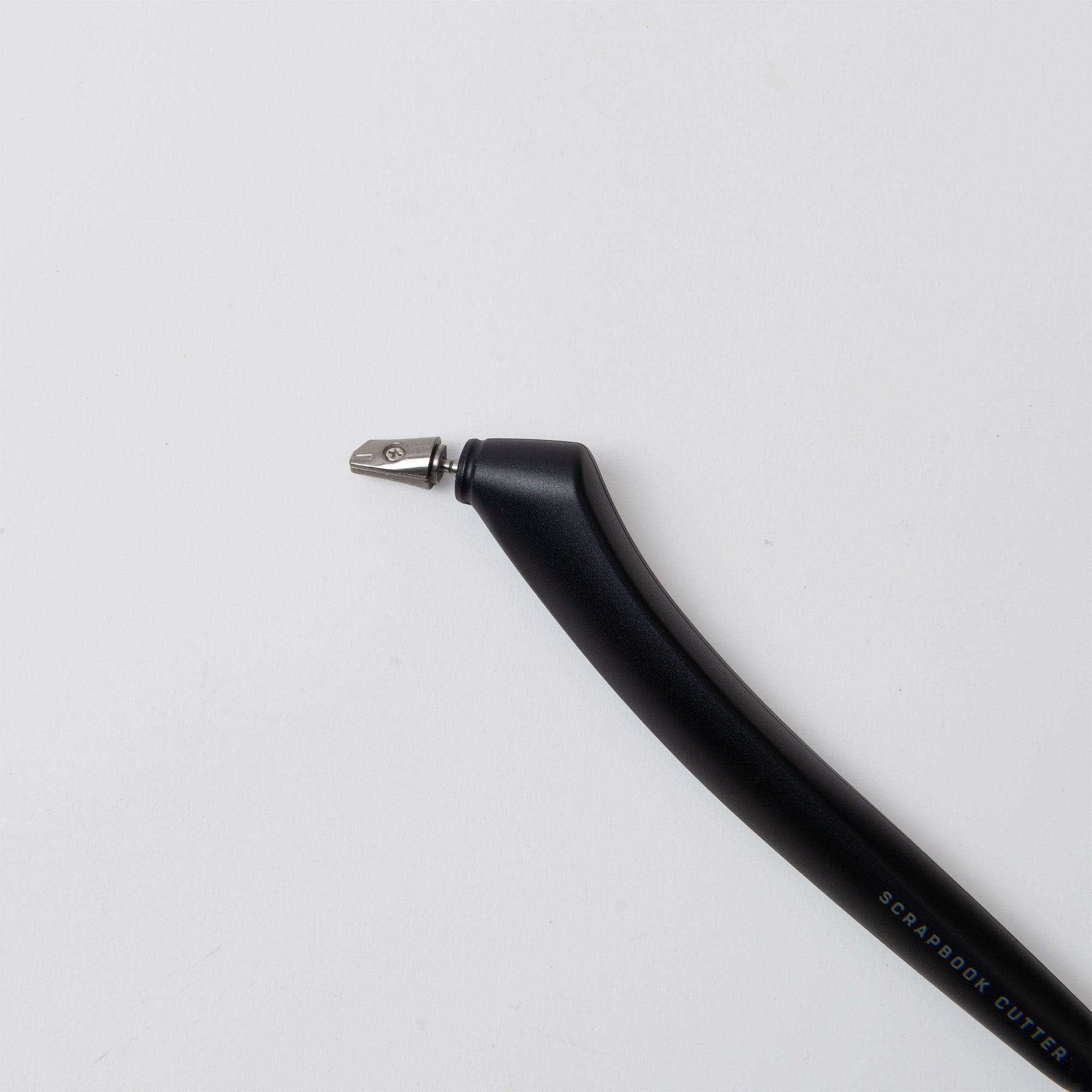 Der Midori Scrapbook Cutter - One Sheet Paper Cutter verfügt über einen geschwungenen schwarzen Griff und eine kleine Keramikklinge, die diagonal auf einem weißen Hintergrund abgebildet ist - ideal zum präzisen Schneiden von Fotos und Papier.