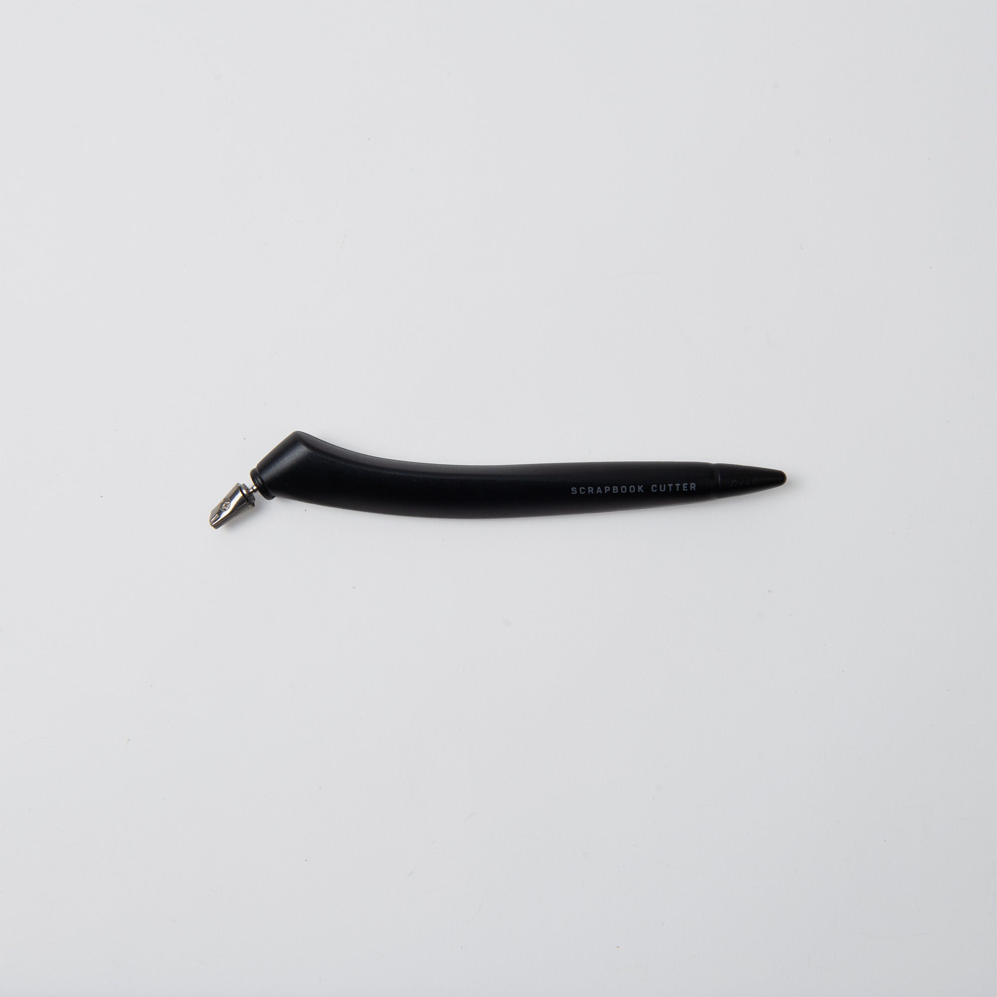 Der Midori Scrapbook Cutter - One Sheet Paper Cutter ist schwarz mit einem gebogenen Griff und einer kleinen silbernen Klingenspitze, die eine 360°-Keramikklinge für präzises Ausschneiden aufweist, dargestellt auf einem schlichten weißen Hintergrund.