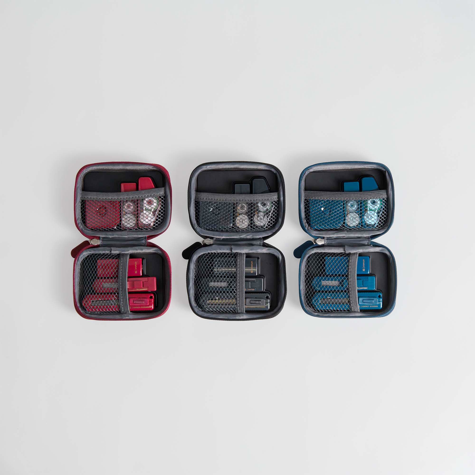 Drei Midori XS Stationery Kits von Midori in den Farben Rot, Schwarz und Blau sind auf einem weißen Hintergrund geöffnet, um ihre organisierten Fächer für Flaschen und Behälter zu zeigen.