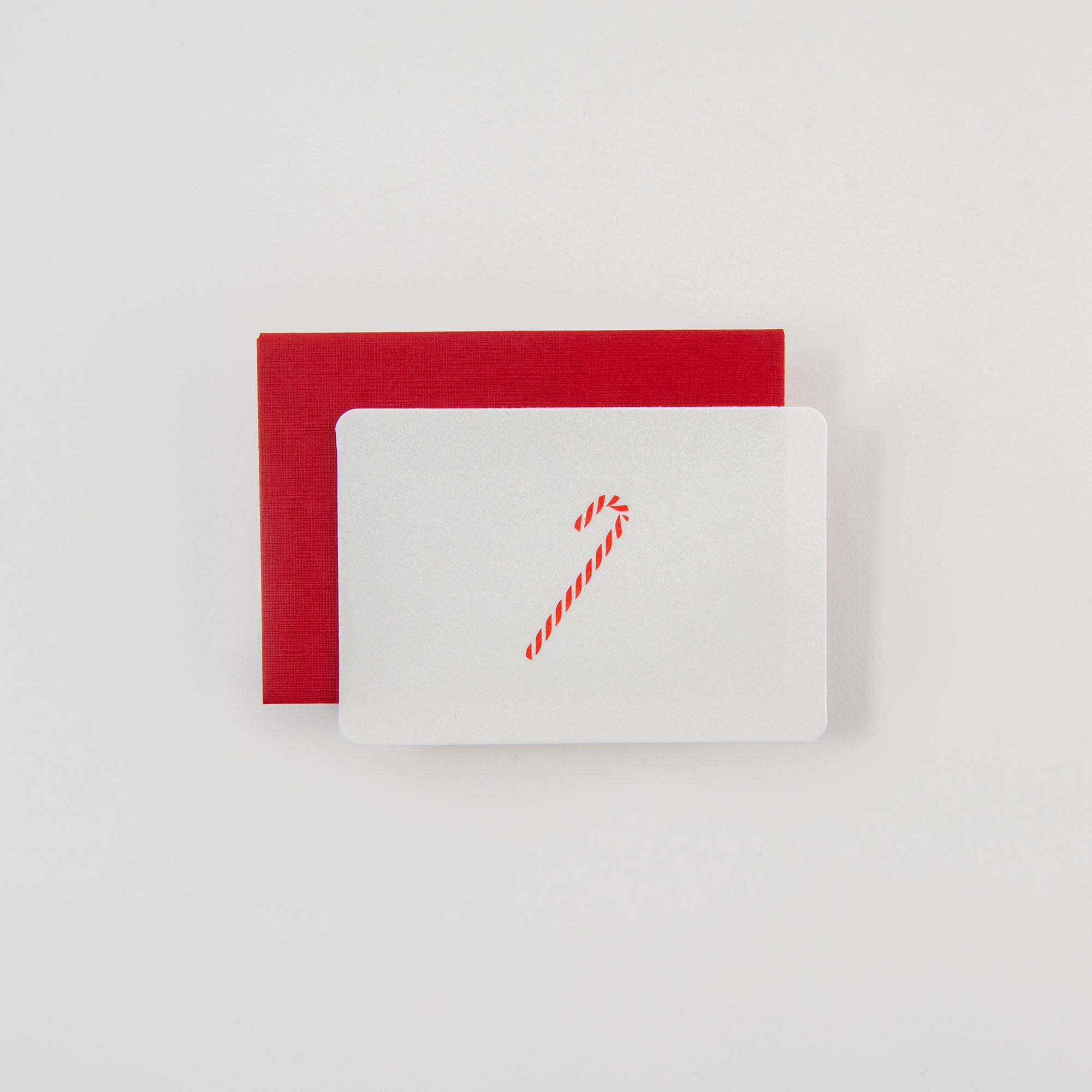 Die Zuckerstange - Mini Karte von Le Typographe zeigt eine rote Zuckerstange auf Weiß und liegt auf einem roten Umschlag - ein festlicher Gruß, der Erinnerungen an Belgien weckt.