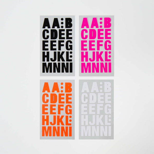 Die selbstklebenden Buchstaben von Paper Poetry bestehen aus vier Grußkarten mit fettgedruckten Großbuchstaben: schwarz (oben links), rosa (oben rechts), orange (unten links) und grau (unten rechts). Jede Karte zeigt die gleiche Buchstabenfolge von „AA: B“ bis „MN: NI“ in atemberaubenden Farbvarianten.