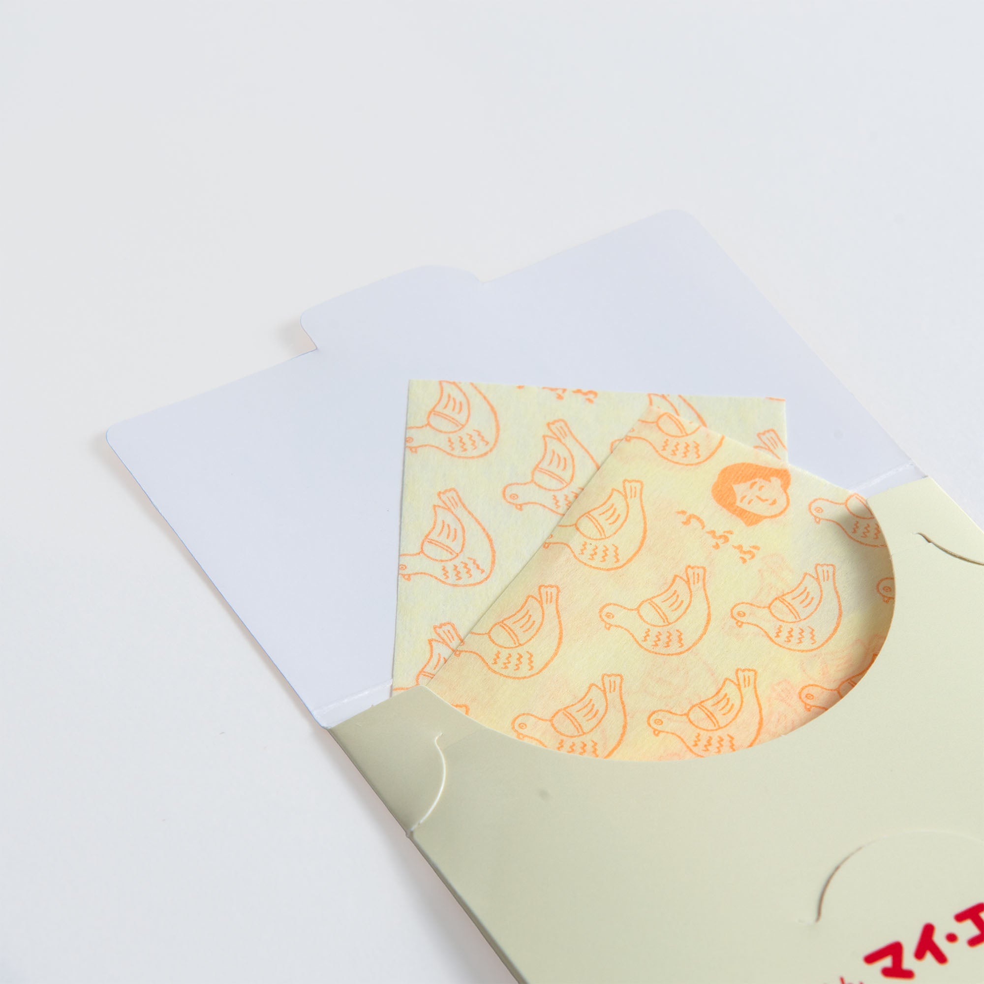 Die Papierseife von Hightide mit orangefarbenen Retro-Vogelillustrationen lugt aus einem cremefarbenen Umschlag mit kreisförmigem Ausschnitt vor weißem Hintergrund hervor.