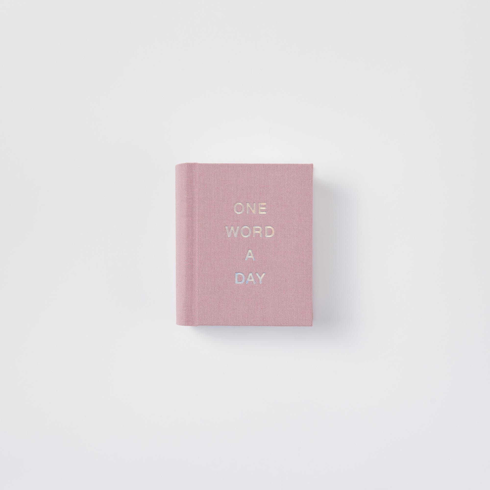 Das paperlux OWAD Elements ist ein kleines, rosafarbenes Leinen-Hardcover-Mini-Tagebuch mit "ONE WORD A DAY" in Goldprägung auf dem Einband - perfekt als Geschenk geeignet und auf weißem Hintergrund abgebildet.