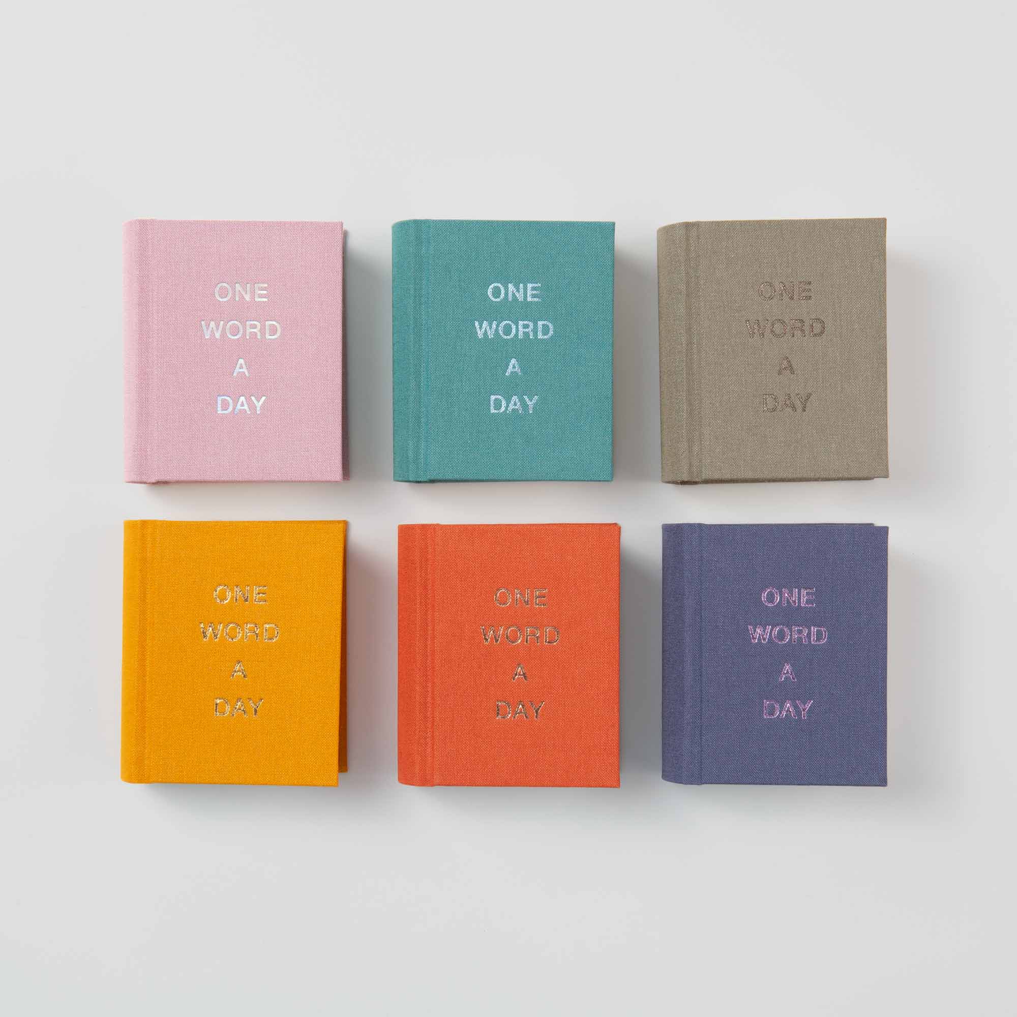 Sechs kleine OWAD Elements Leinen-Bücher von paperlux in Pink, Teal, Beige, Orange, Rot und Lila liegen in zwei Reihen. Jedes Mini-Tagebuch trägt den Aufdruck ONE WORD A DAY - ein ideales Geschenk für jeden Anlass.