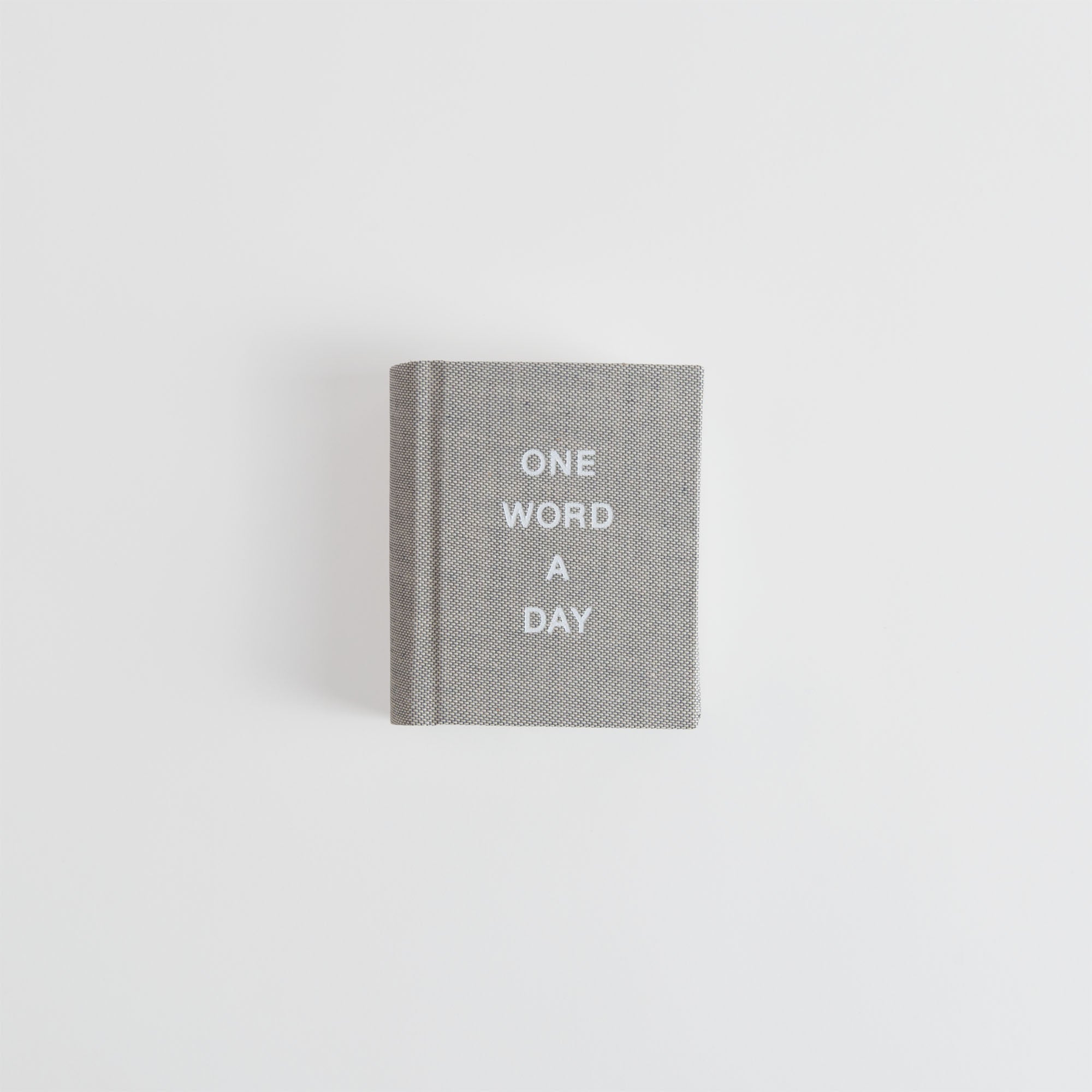 Ein kleines graues OWAD Hygge Collection Tagebuch von paperlux.store mit ONE WORD A DAY in weißen Großbuchstaben auf dem Einband, vor einem schlichten weißen Hintergrund.