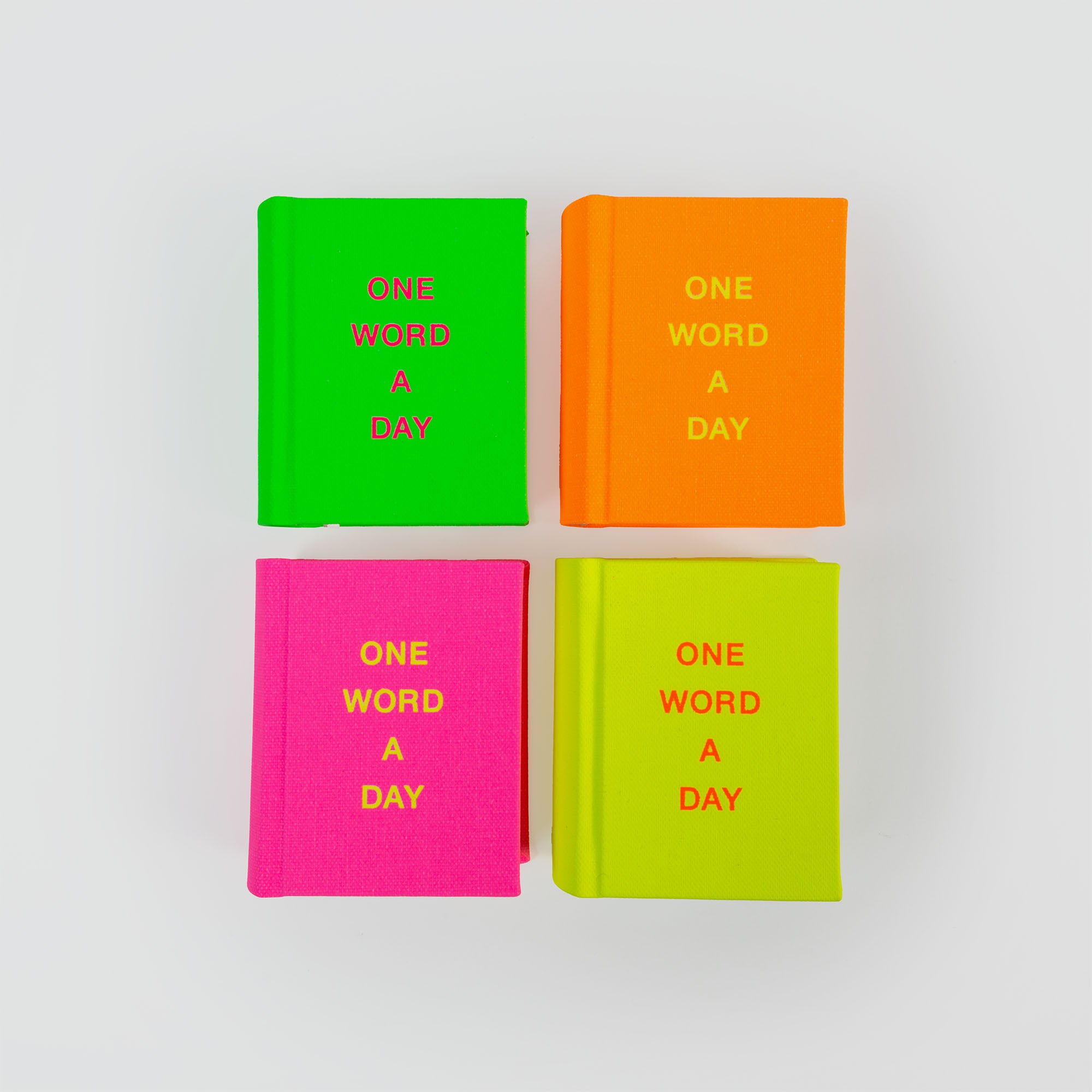 Vier kleine OWAD Neon-Bücher von paperlux in leuchtendem Grün, Orange, Pink und Gelb sind in einem Quadrat auf weißem Hintergrund angeordnet. Auf jedem Einband steht ONE WORD A DAY - ein perfektes Werkzeug für das Tagebuch und eine durchdachte Geschenkidee.