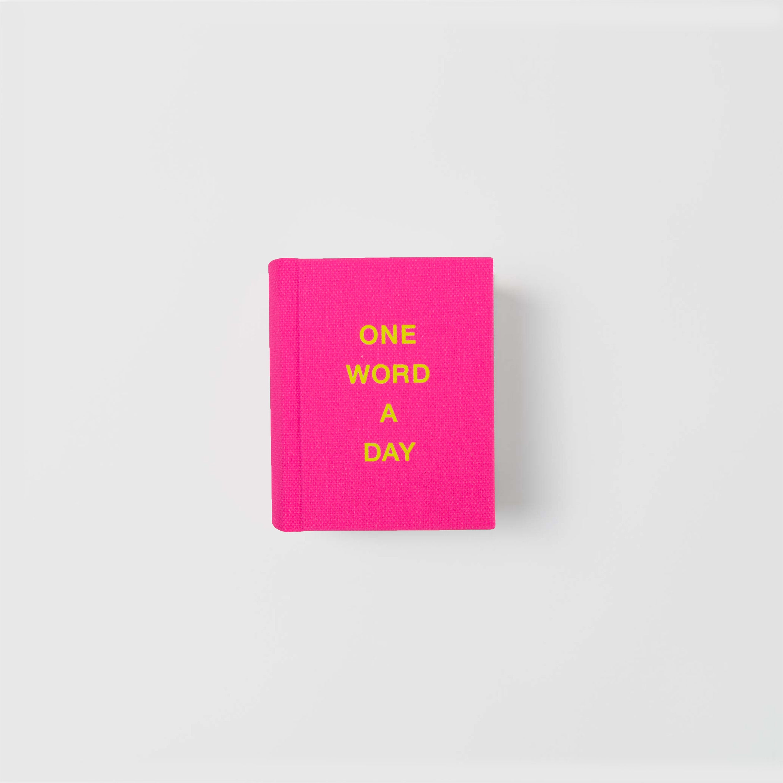 Das OWAD Neon von paperlux ist ein leuchtend pinkfarbenes Buch mit frechem gelben "ONE WORD A DAY"-Text, ideal für Tagebucheintragungen oder als durchdachtes Geschenk, dargestellt auf einem schlichten weißen Hintergrund.
