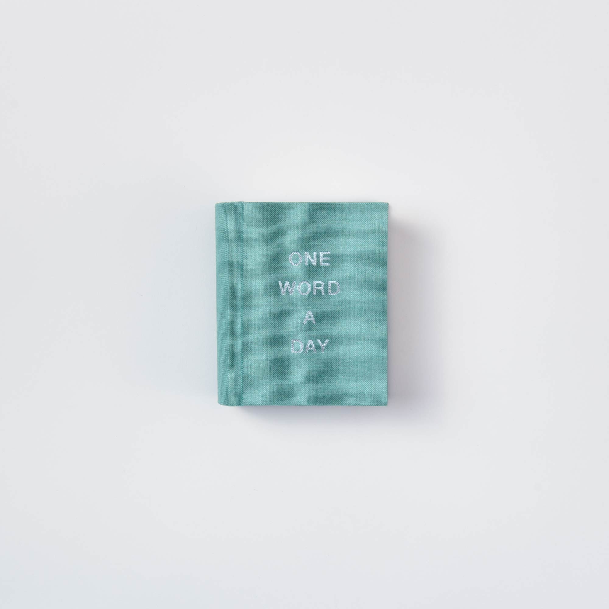 Ein kleines, hellblaues OWAD Elements Leinenbuch von paperlux mit "ONE WORD A DAY" in weiß auf dem Einband, ideal als Geschenk oder Mini-Tagebuch, abgebildet auf einem schlichten weißen Hintergrund.