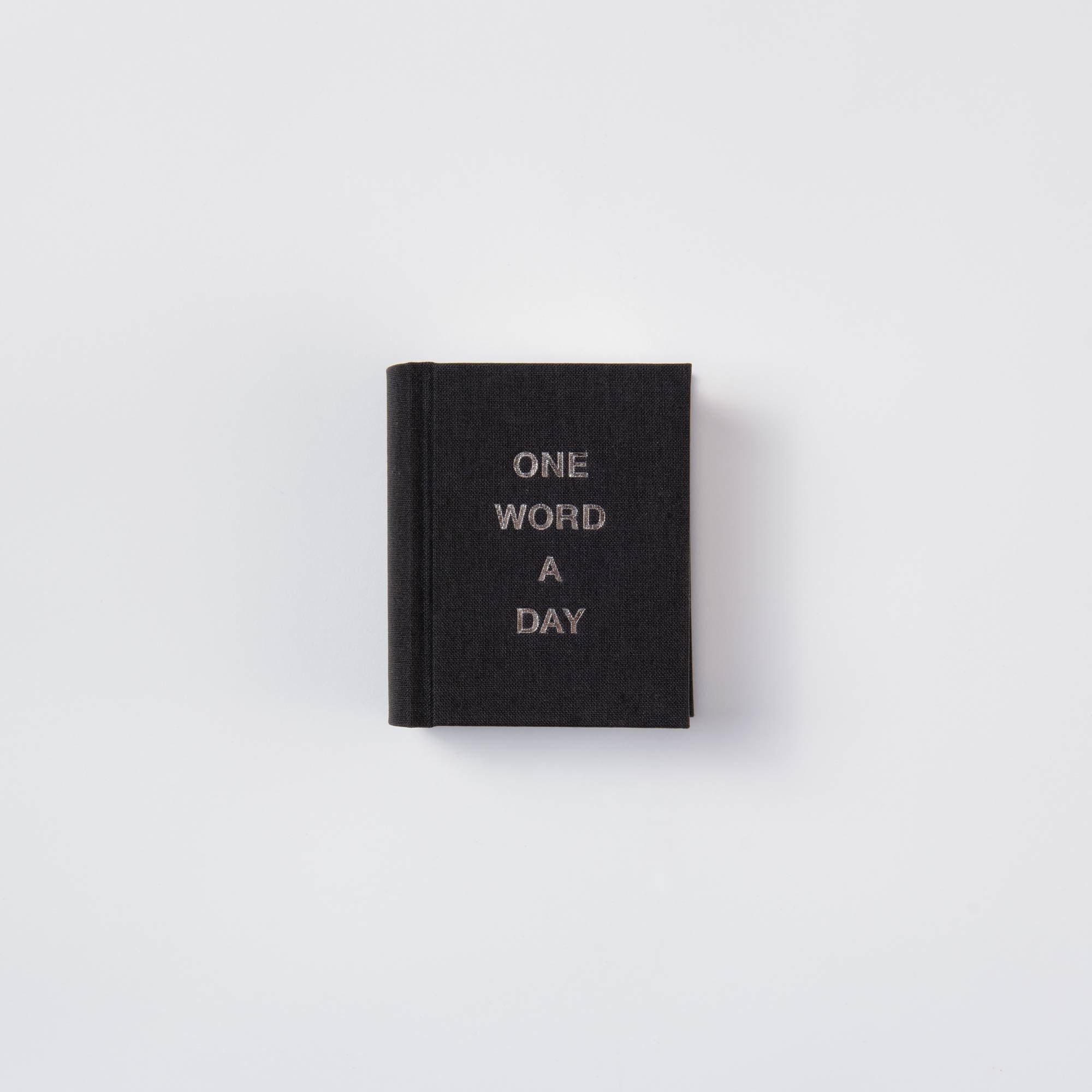 Der paperlux OWAD Klassiker ist ein Mini-Notizbuch mit schwarzem Leineneinband und dem Schriftzug "ONE WORD A DAY" in weißen Großbuchstaben auf dem Einband vor einem schlichten weißen Hintergrund - perfekt als stilvolles Geschenk.