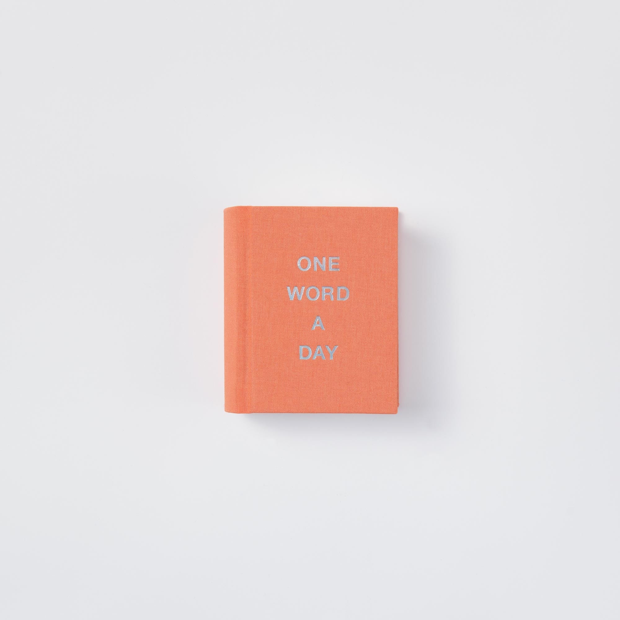 Das paperlux OWAD Shine Bright ist ein orangefarbenes Mini-Notizbuch mit "ONE WORD A DAY" in weißer Schrift auf dem Einband, das sich perfekt als Geschenk auf einem schlichten weißen Hintergrund eignet.