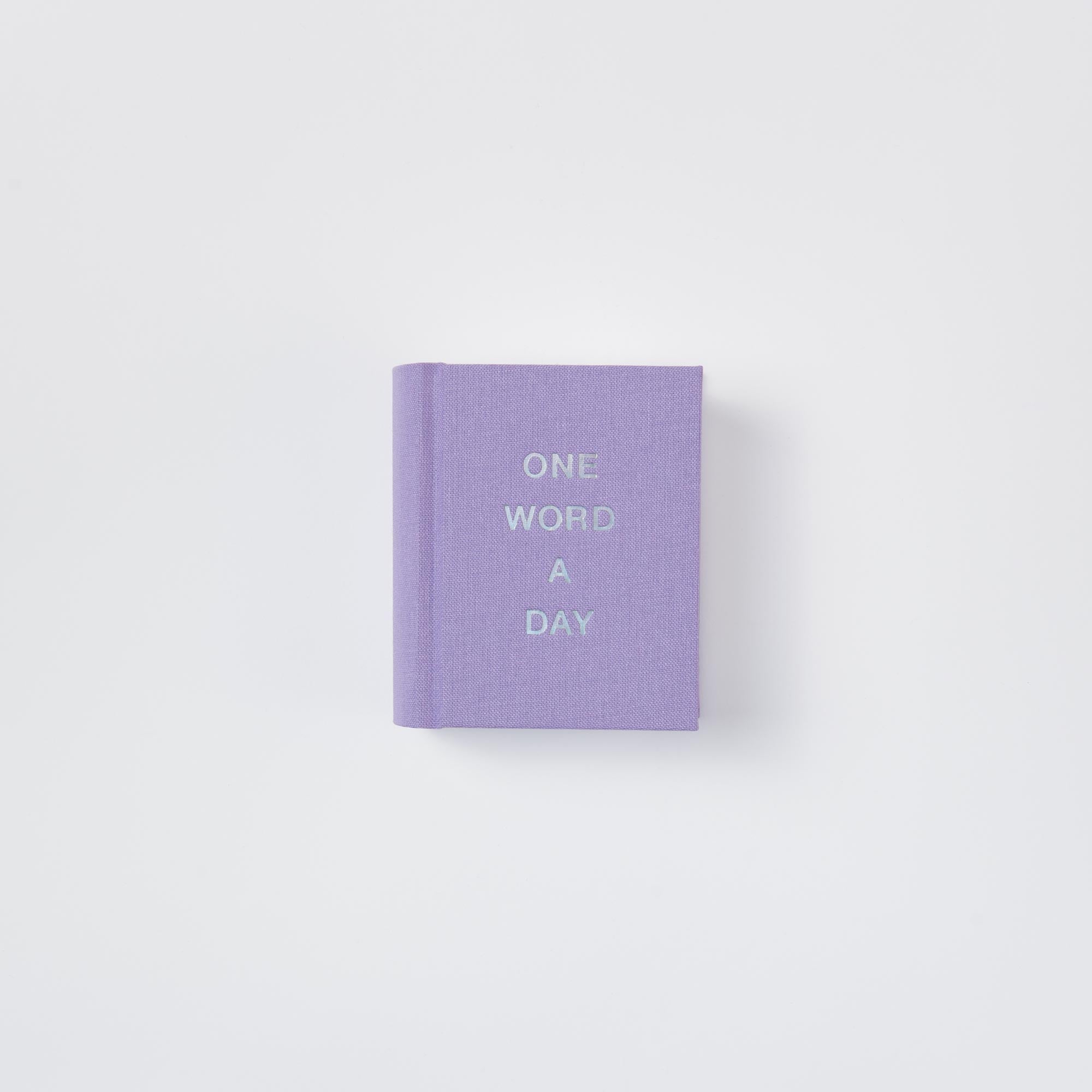 Ein kleines lavendelfarbenes OWAD Shine Bright Mini-Notizbuch von paperlux mit "ONE WORD A DAY" in weißen Großbuchstaben auf dem Cover, fotografiert auf weißem Hintergrund - perfekt als Geschenk für Wortliebhaber.