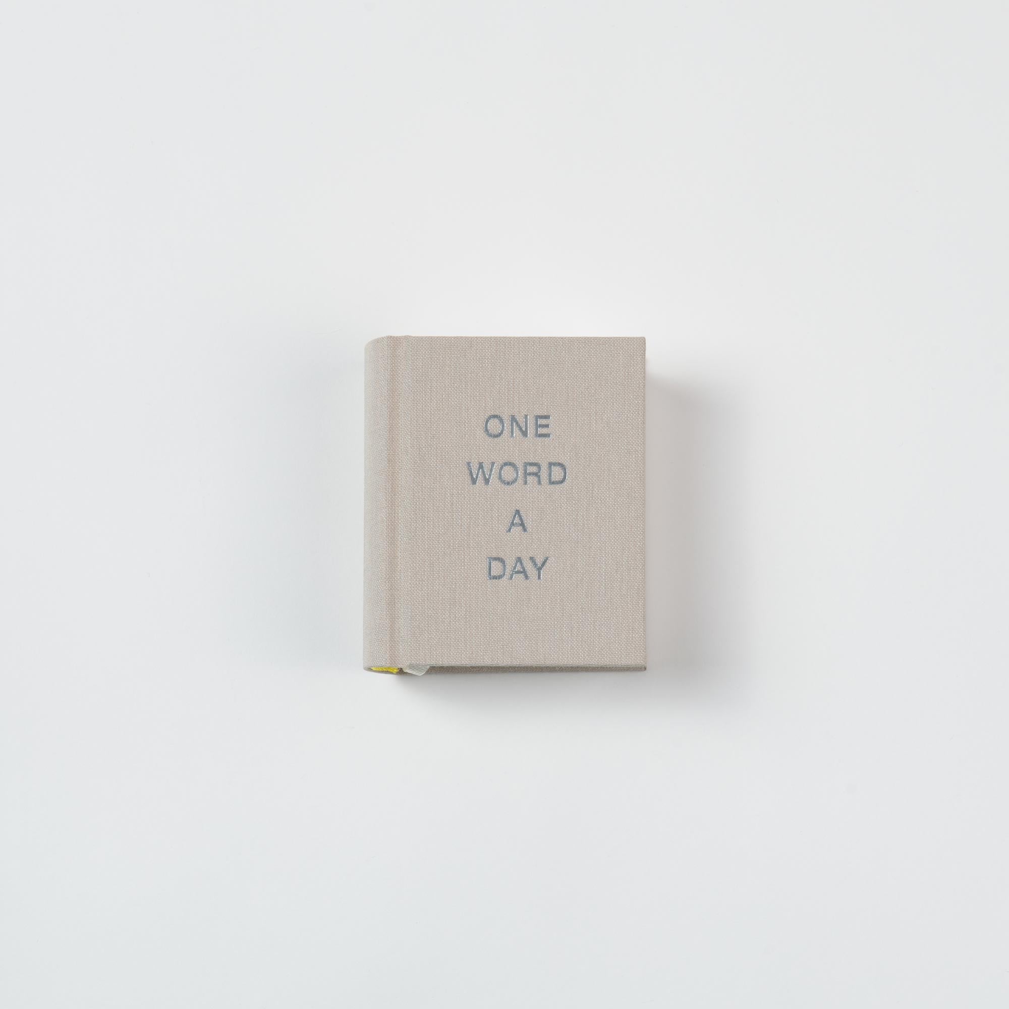 Ein kleines, beigefarbenes, fadengeheftetes Leinen-Geschenkbuch von paperlux mit dem Titel OWAD Urban, mit "ONE WORD A DAY" in grauer Schrift auf dem Einband, fotografiert vor einem schlichten weißen Hintergrund.