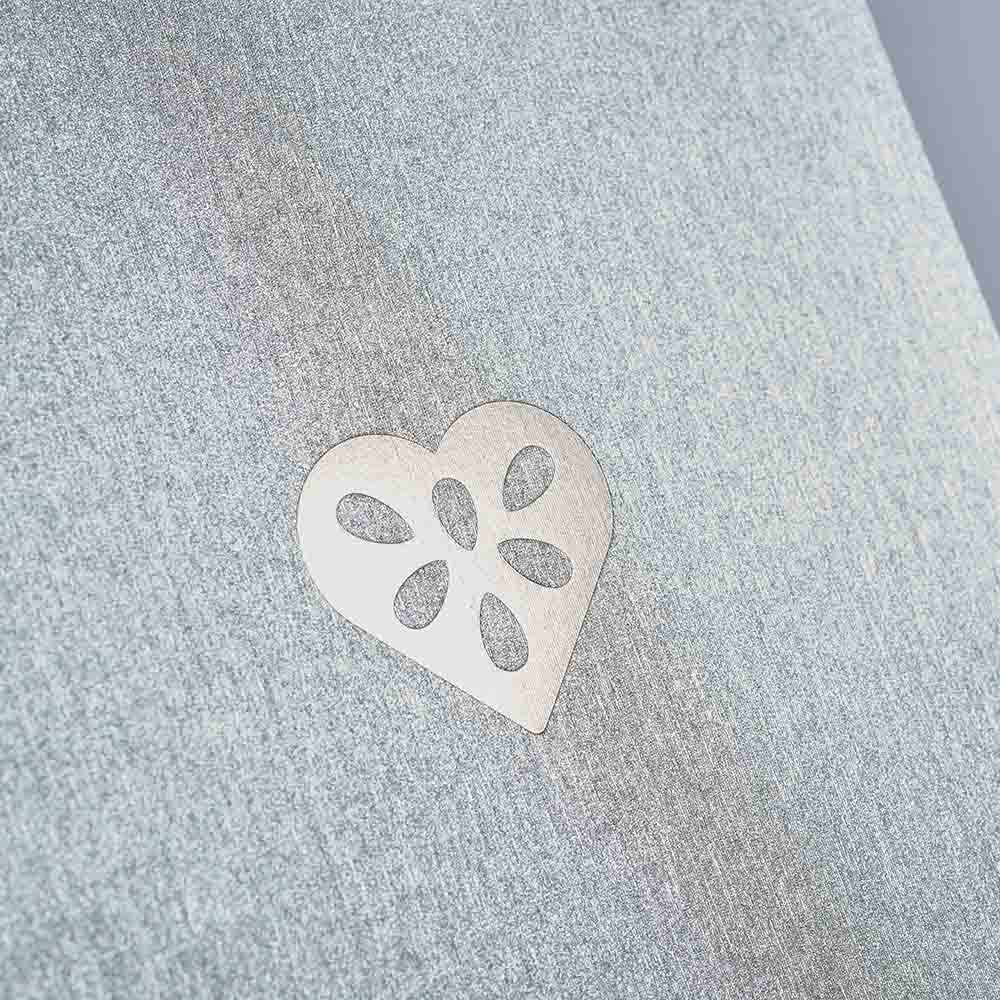 Ein metallischer herzförmiger Ausschnitt mit Blütenmotiven ruht auf einem strukturierten grauen Hintergrund - ideal für das paperlux.store Weihnachtskarten 3er-Set Forest Green, Frost, Silver Dust oder als einzigartige Klappkarte A6 für raffinierte Eleganz.