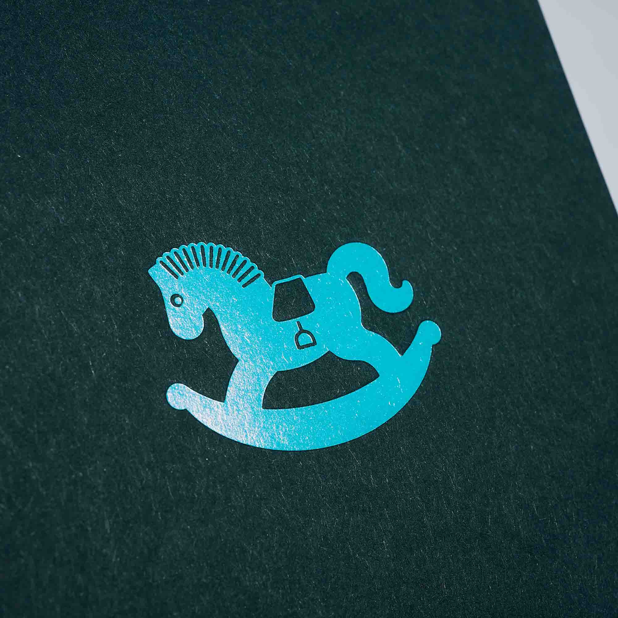 Eine Karte Schaukelpferd von paperlux.store mit einer blauen Schaukelpferd-Silhouette auf dunkelgrauem Hintergrund.
