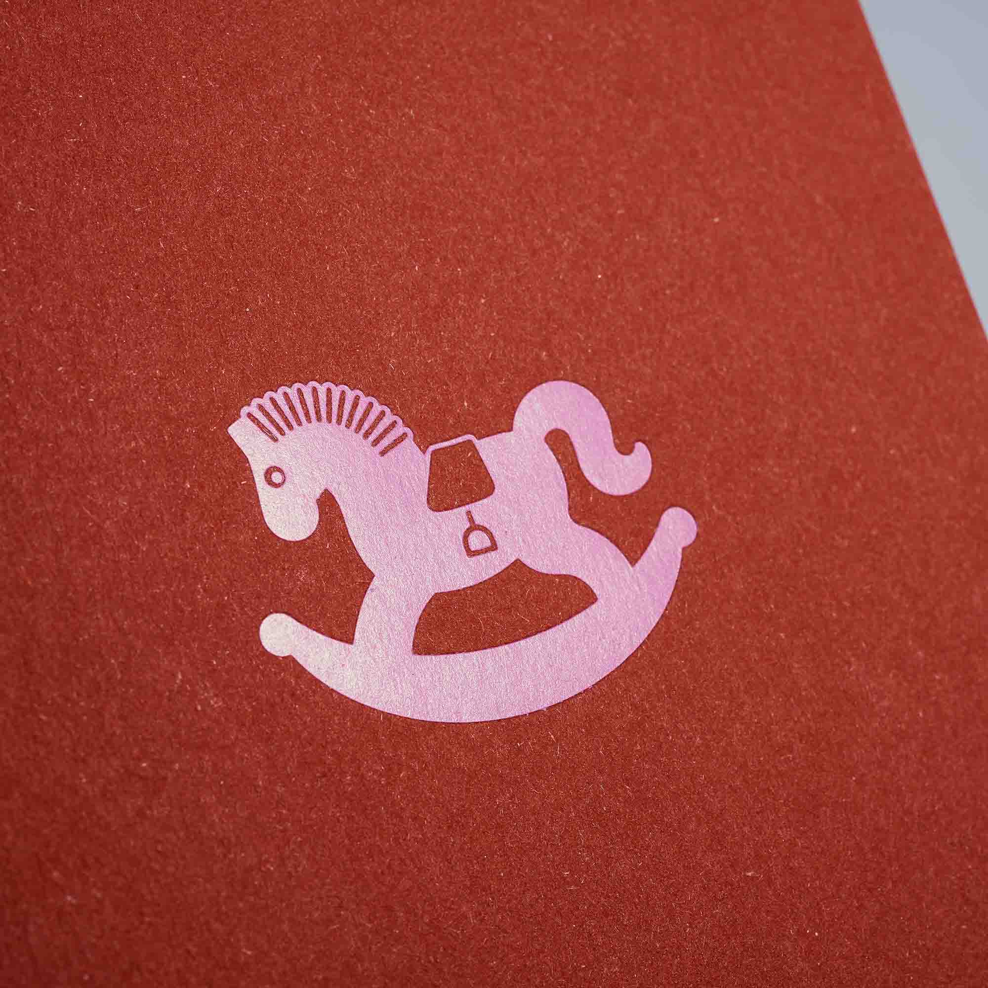 Eine rosafarbene Schaukelpferd-Silhouette ziert die strukturierte rote Karte aus dem Weihnachtskarten 3-er Set Madarine, Silber, Schokolade von paperlux.store - ideal für festliche Grüße oder als einzigartige Klappkarte.