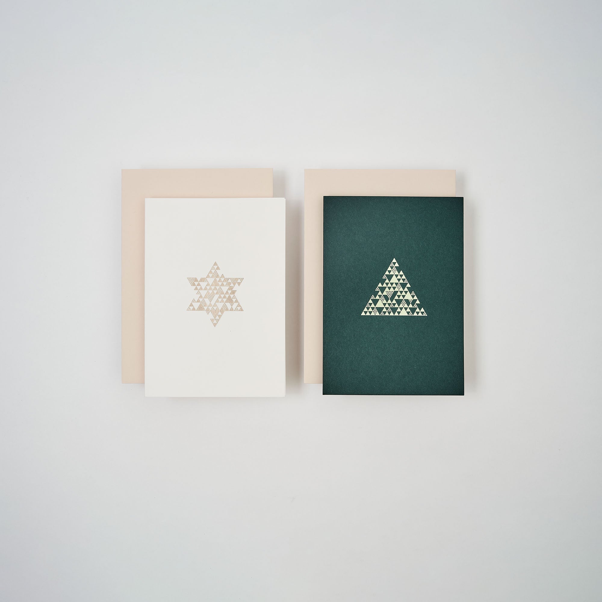 Das Weihnachtskarten 2er-Set Snow & Green von paperlux.store zeigt eine weiße Klappkarte mit Stern und Tannenbaum sowie eine grüne Karte mit Dreiecksmotiv, beide mit beigem Umschlag auf weißem Hintergrund nebeneinander liegend.