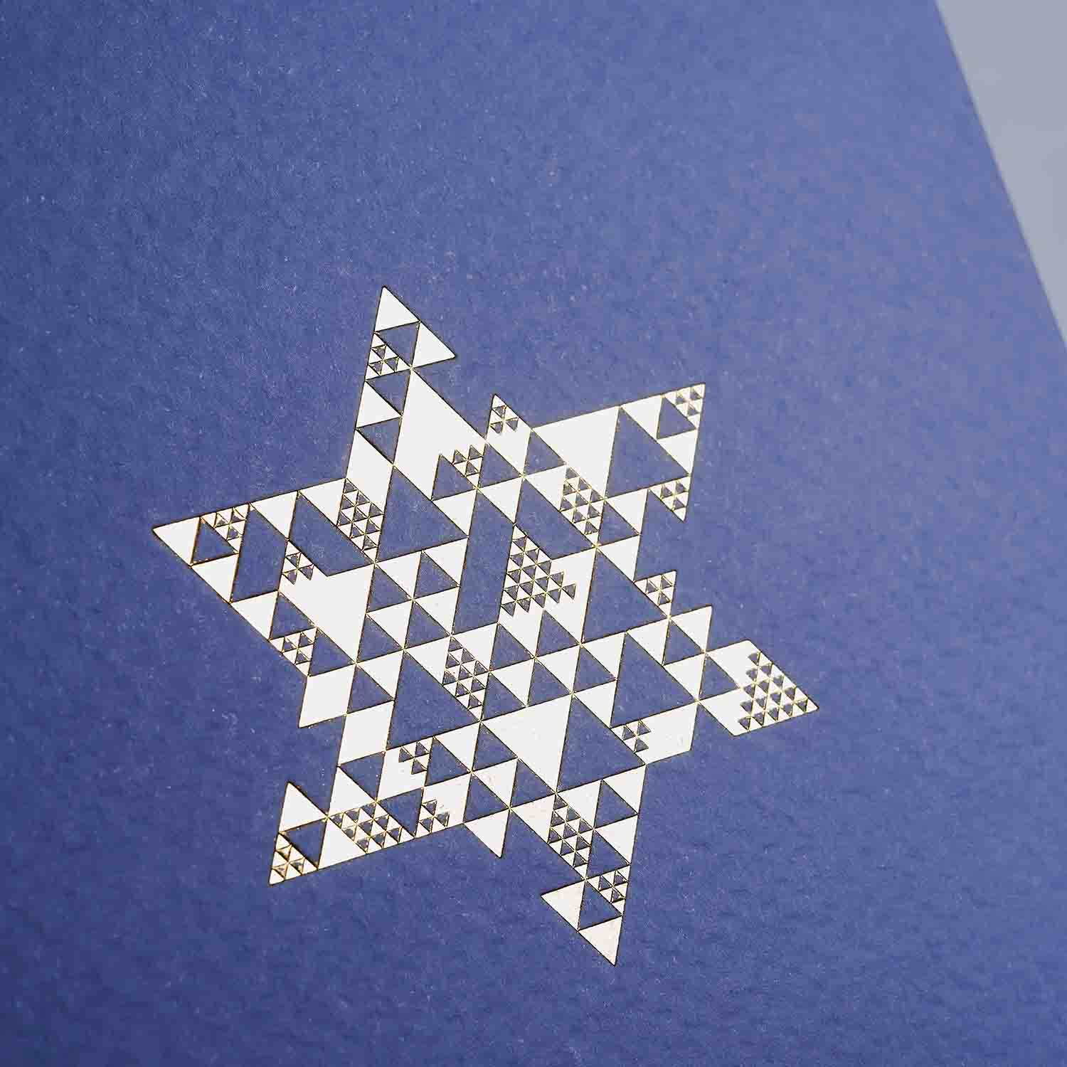 Ein geometrischer Davidstern in schwarz-goldenen Dreiecken erscheint auf blauem Grund im Weihnachtskarten 2er-Set Lavendel & Sage von paperlux.store.