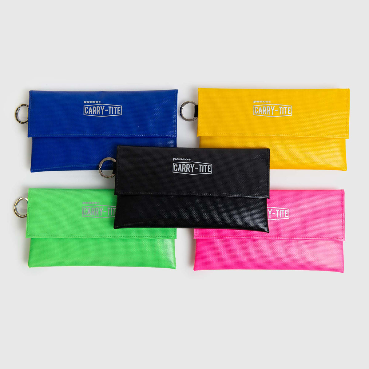 Fünf rechteckige „Penco Carry Tite Tarp“-Stiftetuis in den Farben Blau, Gelb, Grün, Rosa und Schwarz – jeweils aus robustem PVC-Planenstoff gefertigt – sind mit einem Metallring und dem CARRY-TITE-Logo auf der Vorderseite versehen. Diese wasserfesten Etuis von Penco sind übersichtlich auf einem hellen Hintergrund angeordnet.