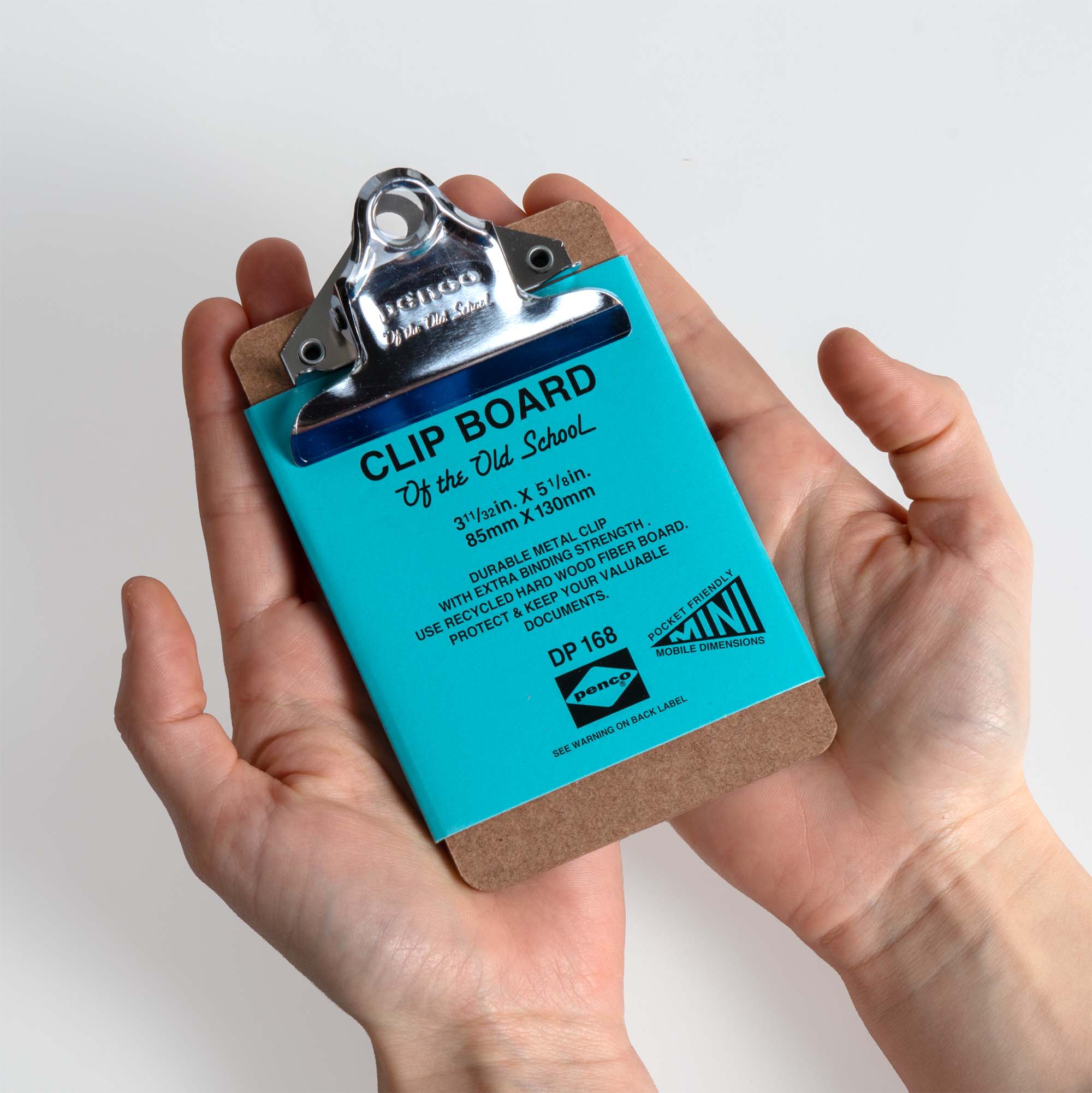 Eine Person hält ein Penco Clipboard XS - Silber mit einem blauen Blatt mit der Aufschrift "CLIP BOARD Off the Old School" und Produktdetails. Dieses Mini-Klemmbrett von Penco hat einen Metallclip und wird vor einem weißen Hintergrund gezeigt.