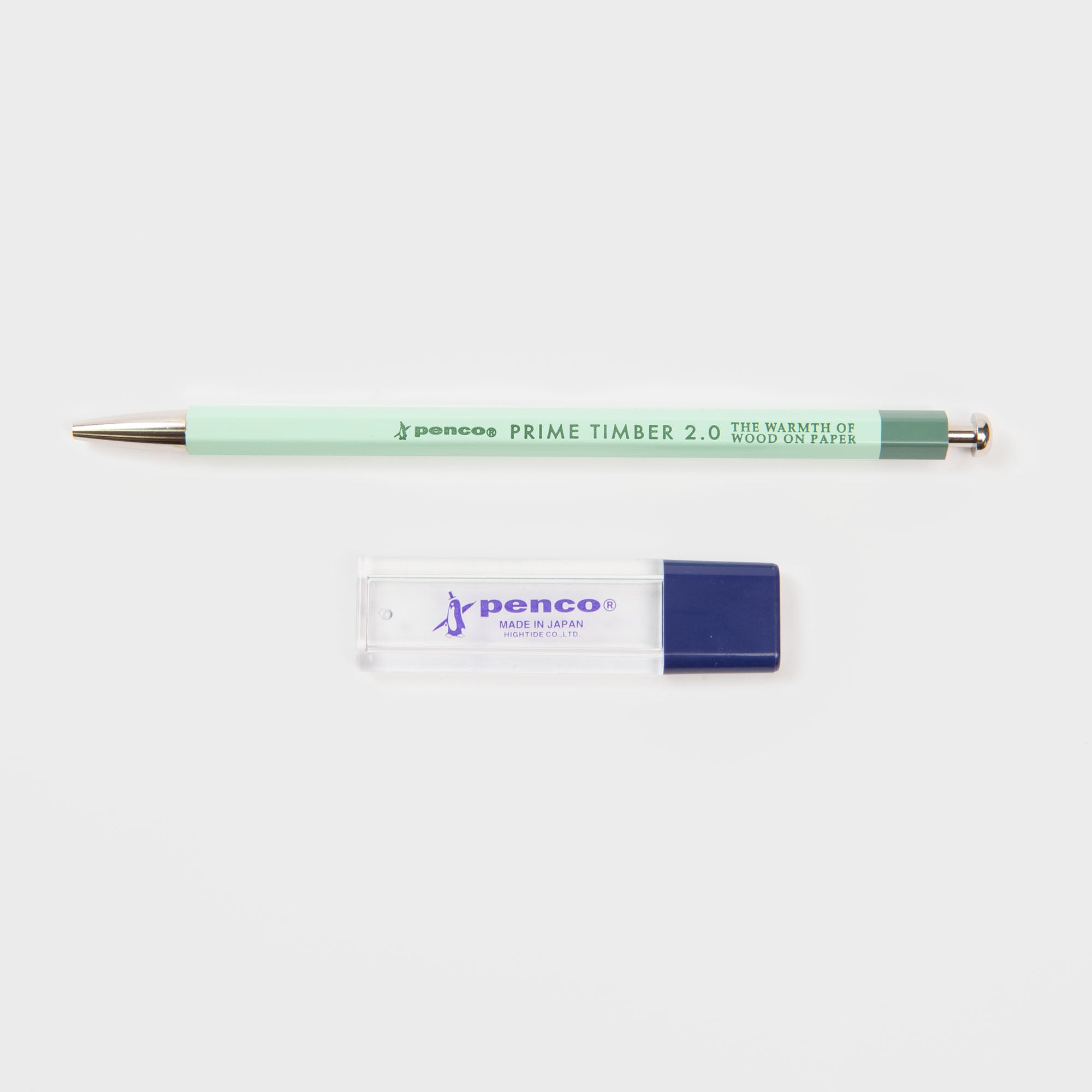 Ein mintgrüner Penco Prime Timber Druckbleistift (2 mm) und ein klarer Anspitzer mit blauer Kappe, beide mit japanischem Design, sind nebeneinander auf weißem Hintergrund platziert.