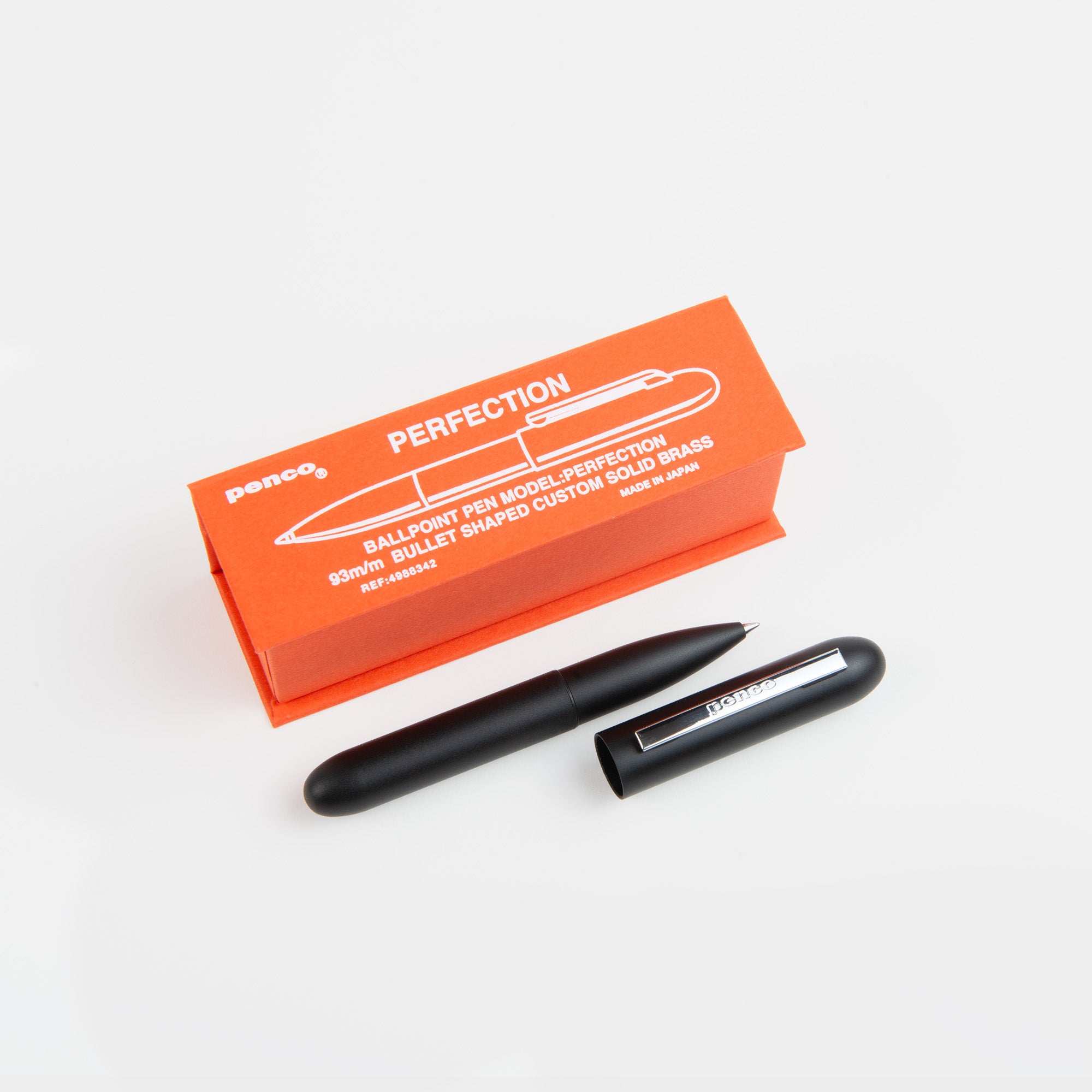Ein schwarzer, kugelförmiger Kompakt-Kugelschreiber - Bullet Pen von paperlux.store ruht vor einer orangefarbenen Box mit der Aufschrift PERFECTION. Er wird in Japan hergestellt und zeichnet sich durch präzises Schreiben und ein schlankes Design aus.