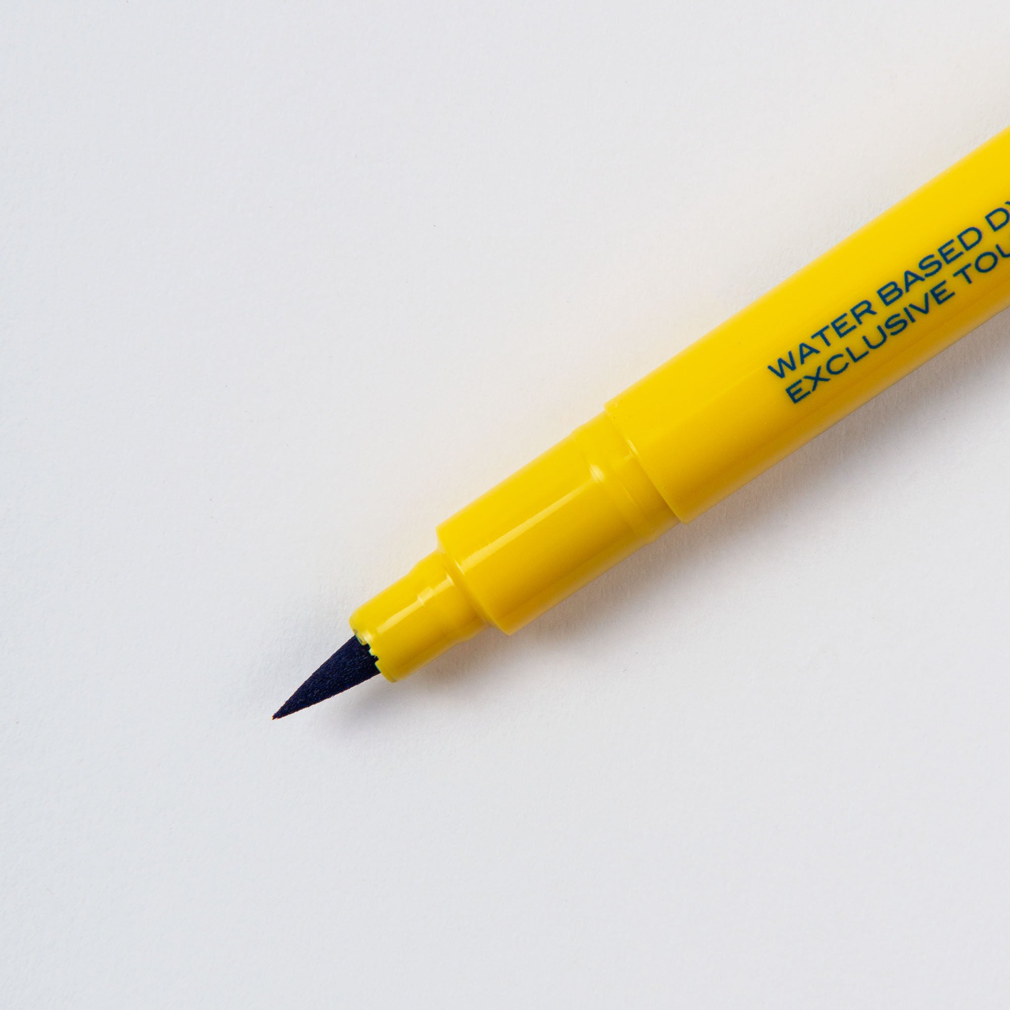 Ein gelber Brushwriter - Kalligrafiestift von Penco mit feiner schwarzer Spitze auf weißem Hintergrund. Auf dem Schaft ist ein kleiner grüner Text „Made in Japan“ als Herkunftshinweis zu sehen.