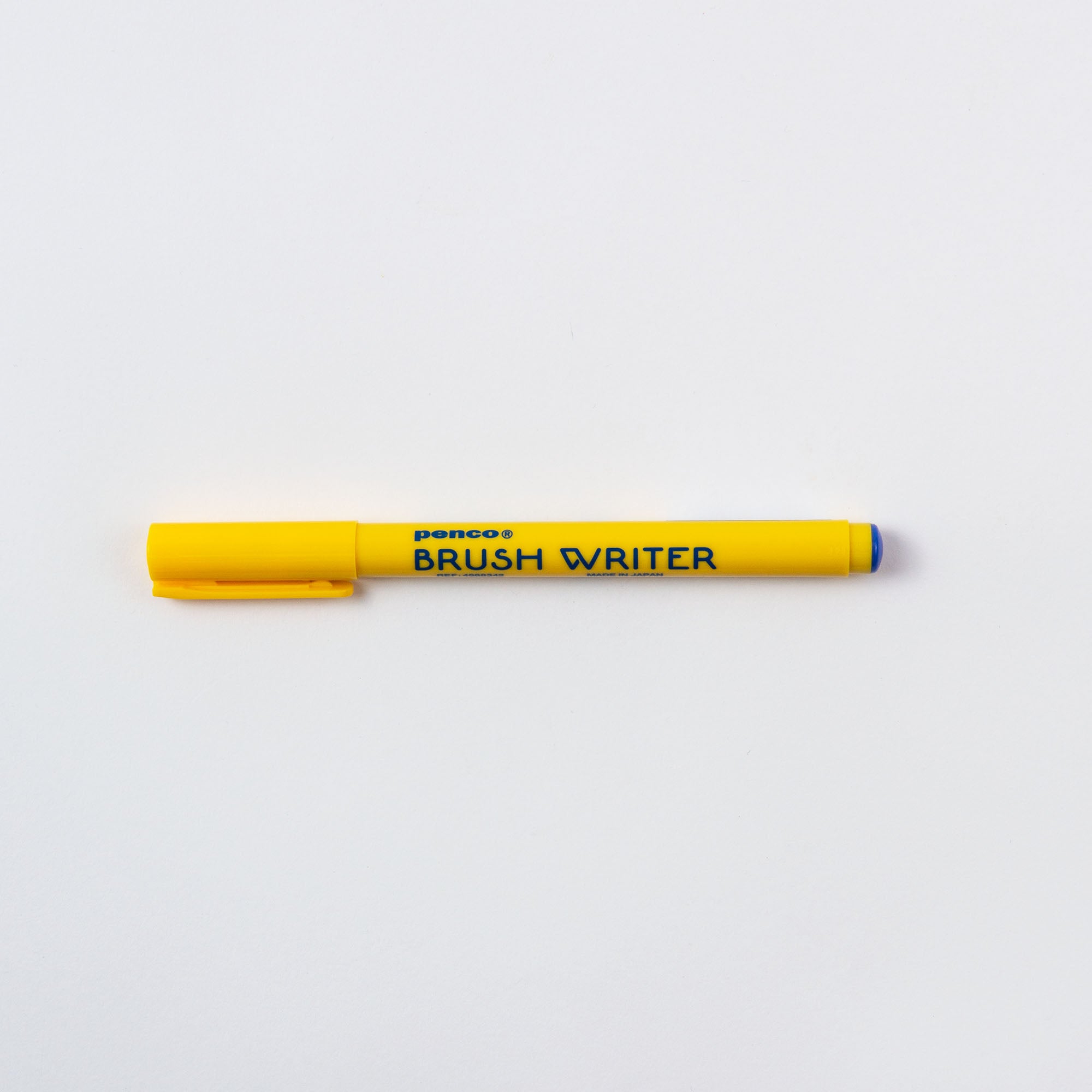 Ein gelber Brushwriter - Kalligrafie-Stift von Penco, hergestellt in Japan, liegt horizontal vor einem schlichten weißen Hintergrund. Er verfügt über eine blaue Spitze und eine passende gelbe Kappe, ideal für angehende Kalligrafie-Pinselmacher.