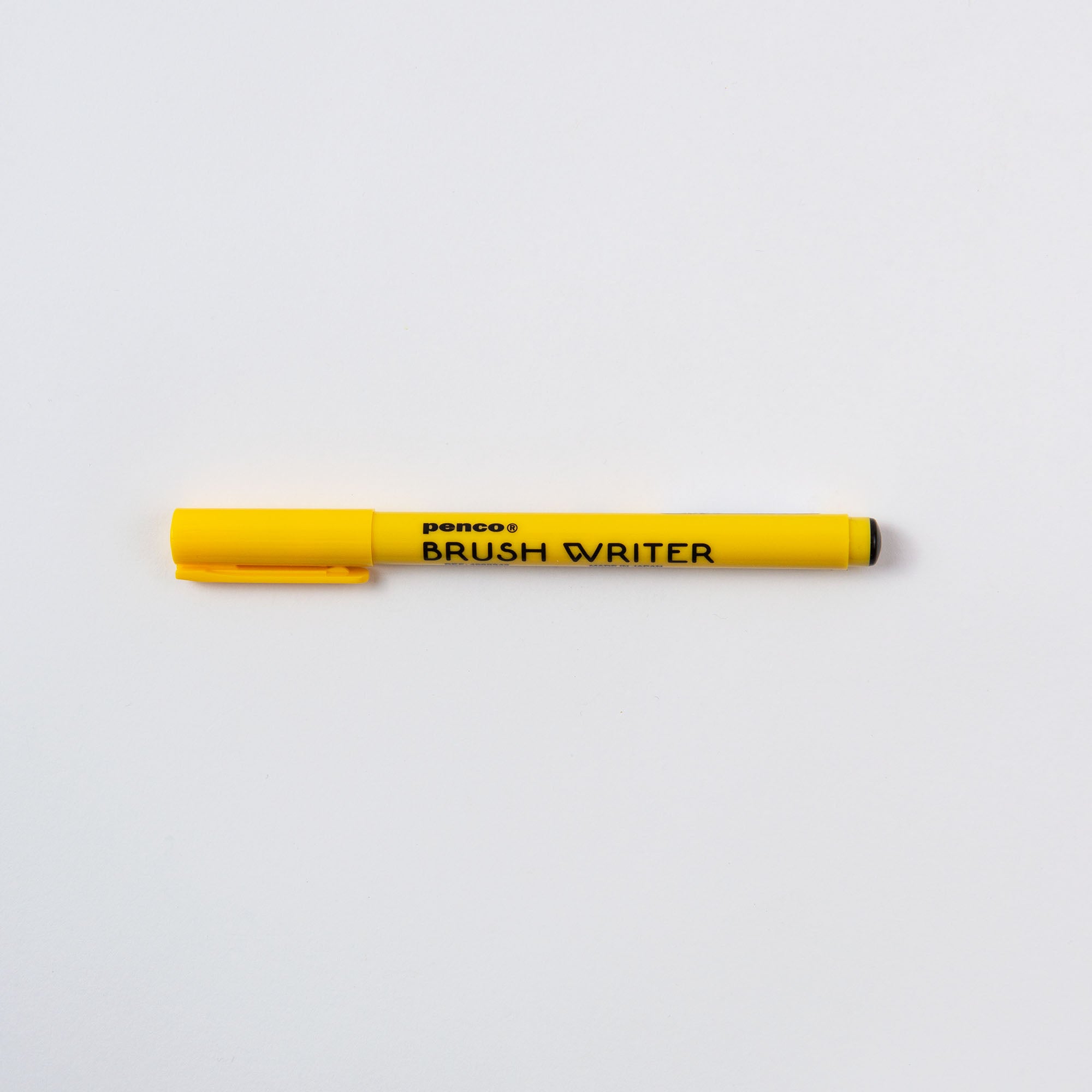 Ein gelber Brushwriter - Kalligrafiestift von Penco liegt horizontal auf einer weißen Oberfläche und trägt die Aufschrift „Penco BRUSH WRITER“ an der Seite. Die Kappe befindet sich auf der linken Seite und wurde von erfahrenen japanischen Kalligrafiepinselherstellern gefertigt.