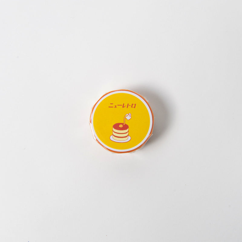 Das Hightide Klebeband - Masking Tape hat ein gelbes, rundes Bonbon-Design mit verspielten Illustrationen, darunter ein Pfannkuchen und japanischer Text. Der klare weiße Hintergrund bildet einen schönen Kontrast zu den lebendigen Grafiken und macht das Auspacken und die Verwendung zum Vergnügen.