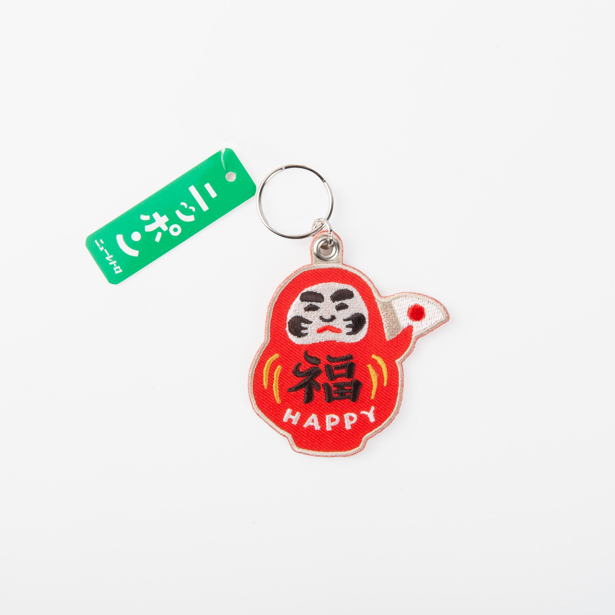 Der Hightide Daruma Schlüsselanhänger - Japanischer Glücksbringer zeigt eine rote Daruma-Puppe mit "HAPPY" und japanischen Schriftzeichen auf dem Bauch sowie einen grünen Anhänger mit japanischem Text auf weißem Hintergrund.