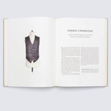 Ein offenes Buch mit dem Titel „Making a Waistcoat“ zeigt das Bild einer schwarzen Weste auf einer Schaufensterpuppe, die die Handwerkskunst des Savile Row Suit von Gestalten Verlag verkörpert. Nähanleitungen sind auf den Seiten 82 und 83 vor einem hellgrauen Hintergrund sichtbar.