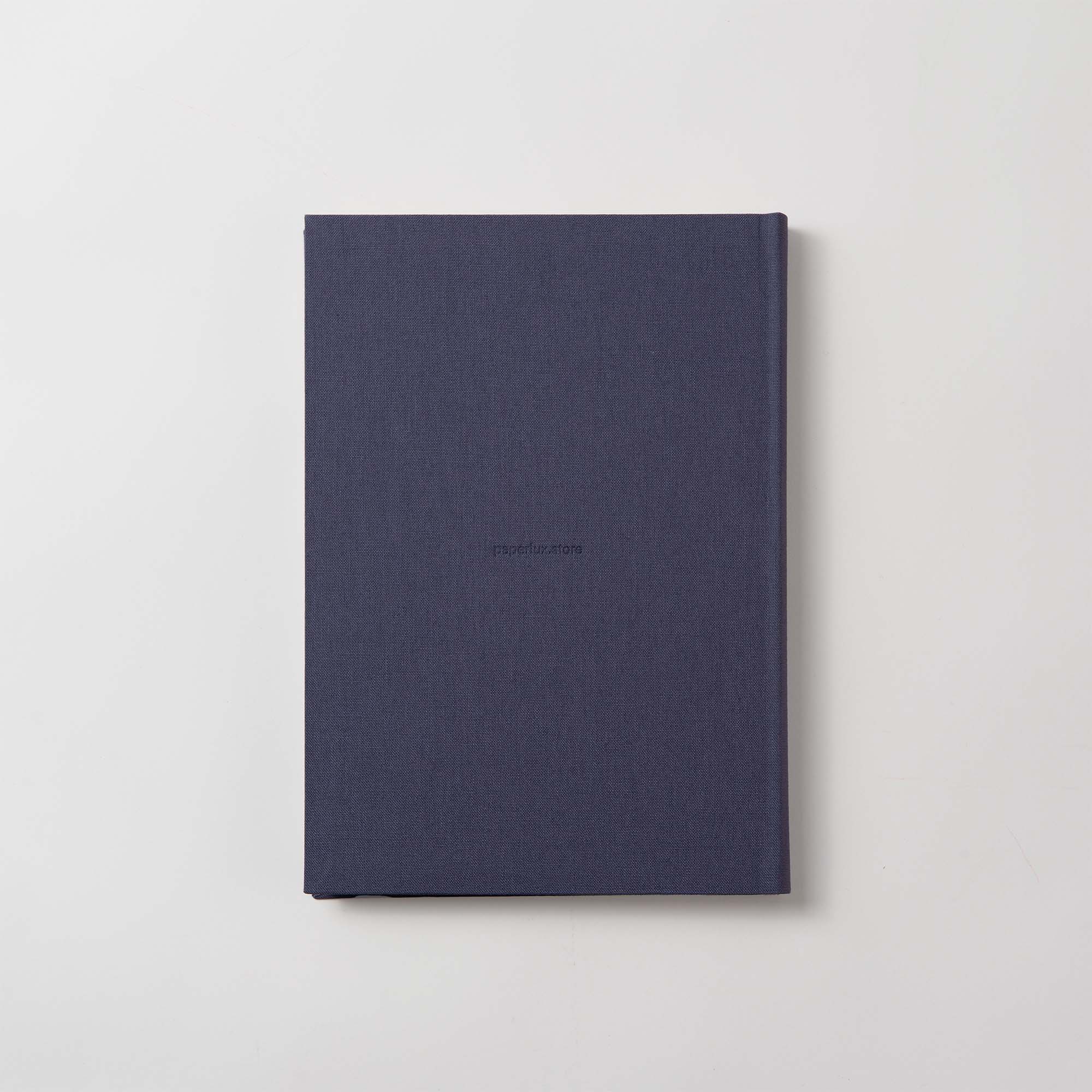 Das Notanizer Notizbuch A5 von paperlux.store ruht elegant auf einer hellgrauen Oberfläche. Sein geschlossener Hardcover-Einband in Dunkelblau trägt in der Mitte das Wort „Reservierungen“ in kleinen schwarzen Buchstaben, während atemberaubende Farbschnittkanten ihm ein modernes Flair verleihen.