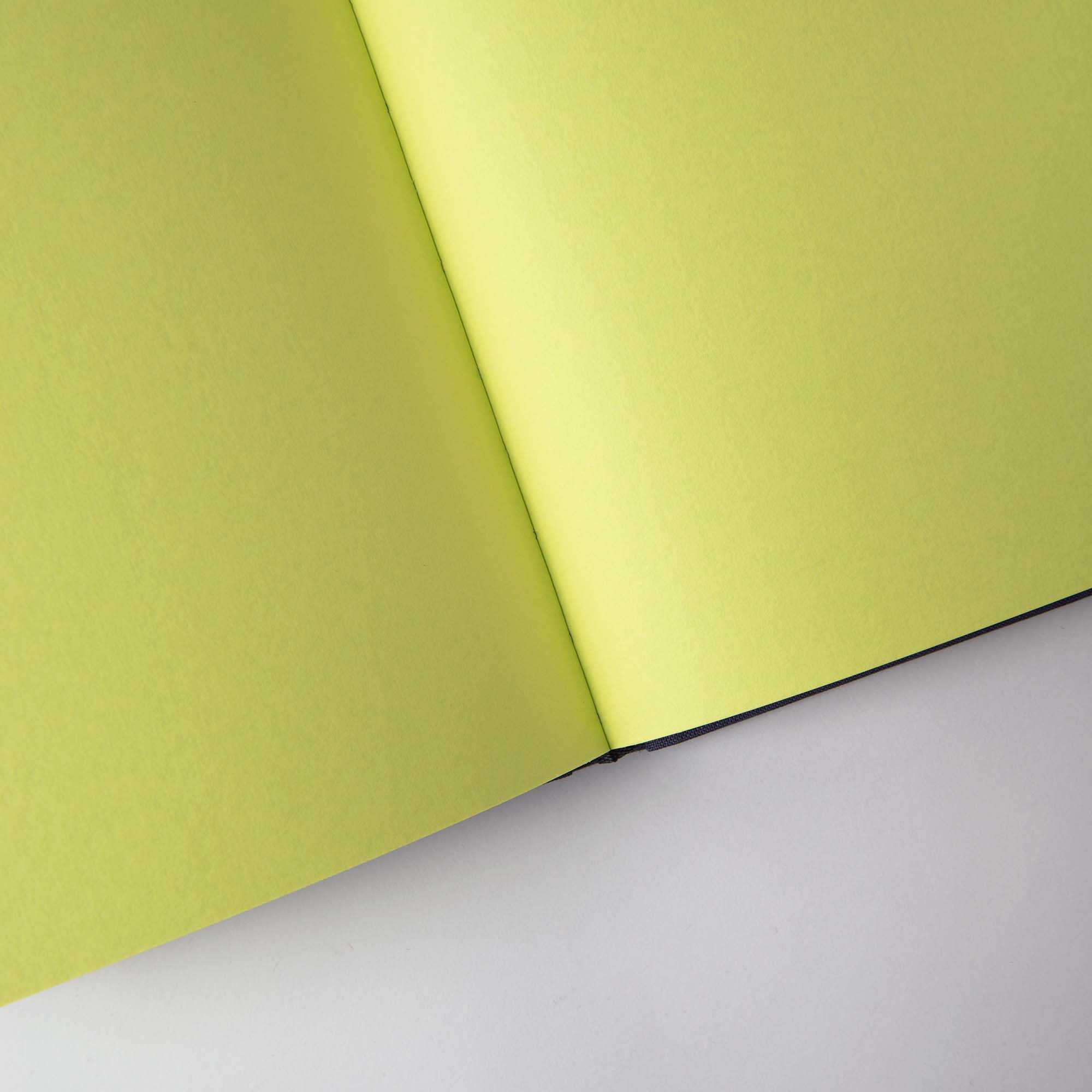 Das Notanizer Notizbuch A5 von paperlux.store mit hellgrünen Seiten aus luxuriösem Feinstpapier wird aufgeschlagen auf einer weißen Fläche in einer gut beleuchteten Umgebung präsentiert.