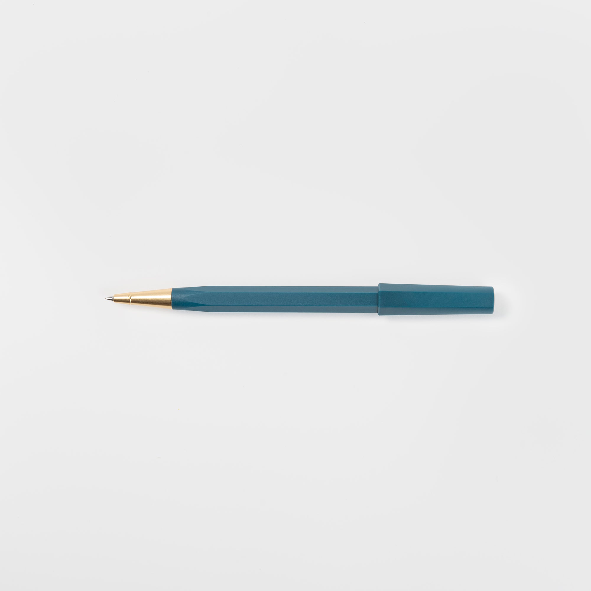 Ein Ystudio Rollerball - Ocean Edition Kugelschreiber mit goldener Spitze liegt waagerecht auf einem schlichten weißen Hintergrund. Die Kappe aus recycelten Fischernetzen ist am hinteren Ende des Stiftes befestigt.